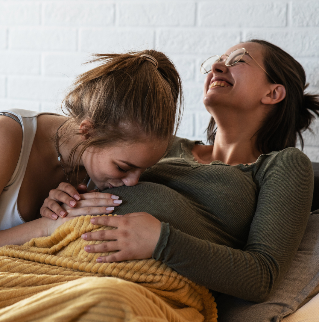 Woman kissing other woman's pregnant belly
